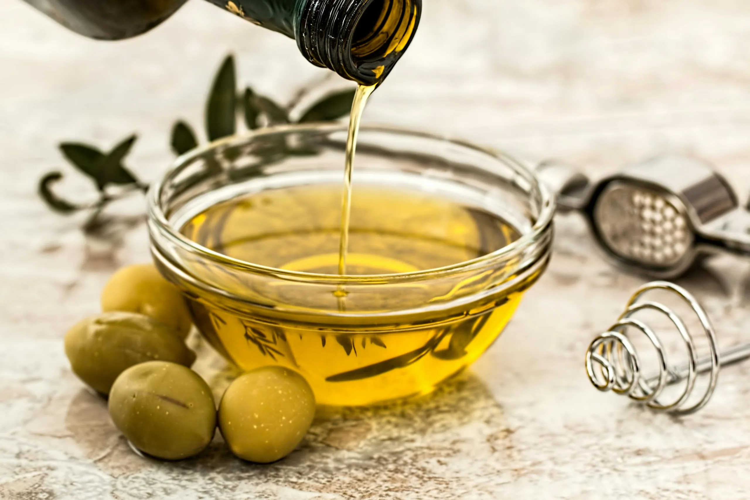 Extra virgin olive oil being poured into a glass bowl surrounded by fresh olives